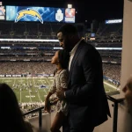 Trevon Diggs walking down stairs with daughter beside him near Dallas Cowboys stadium at halftime and Chargers logo on deck