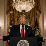 President Trump stands at the podium with light illuminating the Diplomatic Reception Room and an American flag pattern.
