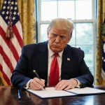 President Trump signs executive order with pen in hand and flag backdrop at White House