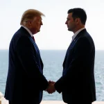 Trump and Zelenskyy clasp hands at Mar-a-Lago entrance with warm lighting and ocean backdrop.