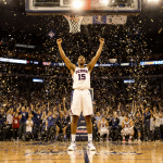 UConn player celebrates victory with arms raised and confetti falling as bright court lights illuminate the scene