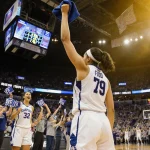 Azzi Fudd raises an arm with the UConn basketball audience waving blue and white towels and scoreboard 79-51 in the backgroun