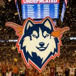 UConn logo shines with Texas logo above and confetti-filled arena filled with cheering fans