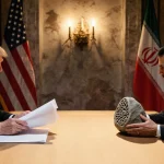 Iranian delegate holds stone while U.S. representative holds papers with flags behind them in a dusk-lit UNSC hall.