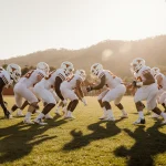 UT Austin Longhorns practice football on sunny field with coaches watching and green hills in background