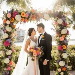 Venus Williams and Andrea Preti pose at a floral arch with peonies and palm trees on a Palm Beach wedding backdrop.