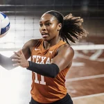Torrey Stafford spikes volleyball with Texas Longhorns jersey and muscles highlighted on blurred court