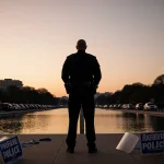 Police chief standing on Washington D.C. National Mall with light behind reflecting pool and riot shields in foreground.