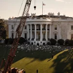 Construction crane stands sentinel with warm sun glow on White House East Wing and scattered debris