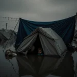Submerged tent floating in murky rainwater with infant silhouette hidden under tarpaulin