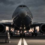 Airplane nose section dominates view with wings obscuring and long spotlight shadows over Washington DC cityscape