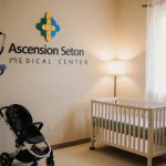 Baby crib softly illuminated in nursery with stroller foreground and hospital logo backdrop.