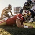 Brock Purdy lying on field with arm outstretched face in shadow with injury and shock with blurred Seahawks defenders behind