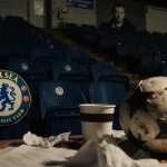 Worn football sits on cluttered desk with crumpled papers and abandoned coffee cups and faint shadow of Enzo Maresca in a mel