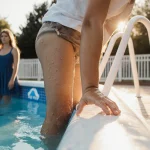 Child gripping pool railing with wet hand while adult looks down for drowning warning