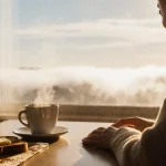 Person sits at kitchen table sipping coffee with buttered toast and cinnamon in a cozy Sunday morning setting
