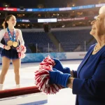 Debbie Bowe holds blue gloves with pom-poms while Brittany Bowe stands on Olympic podium under golden light in arena rink.