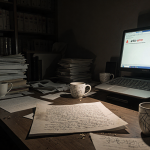 Flickering screen illuminates manuscript with crossed‑out equations on cluttered desk with error message in background