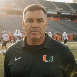 Miami Hurricanes coach Mario Cristobal addressing his team on the sidelines with stadium gridiron and golden light