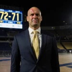 Micah Shrewsberry coach standing outside Notre Dame arena with clenched jaw and score 72-71 on display.
