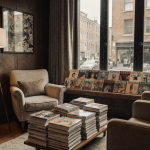 Reader sits in cozy armchairs reading magazines with natural light from large windows and cityscape outside