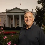 Gary Walters standing before the White House with lush greenery and flowers at sunset.