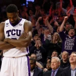 James Nnaji crosses arms with frustration as coach signals substitution after foul and bench watches while TCU crowd in red g