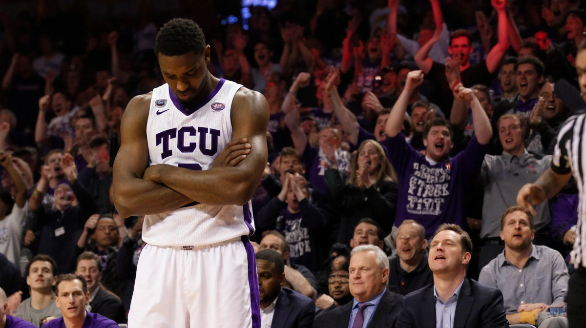 James Nnaji crosses arms with frustration as coach signals substitution after foul and bench watches while TCU crowd in red g