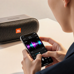 Hands adjusting JBL BandBox Solo speaker with smartphone waveform of rock guitar solo