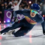 Jordan Stolz falling on the ice with speedskating skates and a spotlight on his face with LED lights reflecting around him