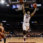 Josh Hubbard shoots a three-point basketball shot in overtime with scoreboard reading 101‑98 and fans cheering in background