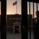 Security doors open at MDC Brooklyn showing Maduro and wife in shadows with warm dusk light and flag