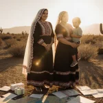 Women in Mexican clothing stand together with a child under golden light holding documents and maps that convey solidarity.