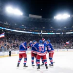 Mika Zibanejad raising his stick in hat trick with Rangers teammates cheering around him on a floodlit rink