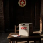 Worn chair holding slightly ajar ballot box with USDP logo in background and soft warm lighting casting long shadows.