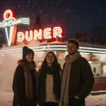 Friends bundled up stand in front of neon diner with foggy winter night on New Year