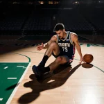 Nikola Jokic twisting his leg with an injured knee and a basketball near his hand in a dimly lit Miami arena.