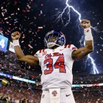 Trinidad Chambliss raises arms with confetti and champagne in front of a 39-34 scoreboard and flashing stadium lights