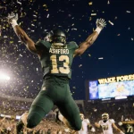 Robby Ashford leaping with arms outstretched after touchdown with confetti falling and Wake Forest logo shining in dark blue