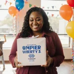 Single mother smiling while holding a charity gift with bright balloons and joyful children nearby