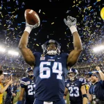 SMU football team celebrates by hoisting the victory ball with Kevin Jennings arms raised and confetti raining over fans in y