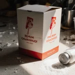 Takeout meal box sits on messy counter with spilled salt crystals catching light and food containers nearby