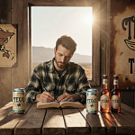 Person sitting at rustic wooden table reading dusty book with Tejas Tonic bottles under golden hour light