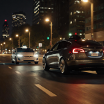 Tesla vehicle trailing behind Robotaxi at night with streetlights casting shadows and a light trail.