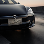 Tesla car parked with bold metallic sign Tesla Full Self-Drive Subscription on dashboard and dim glow from navigation screen