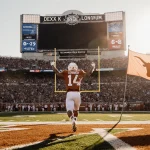 Longhorn football player running out of end zone with arms raised with Texas flag waving behind and scoreboard showing 10-3 r