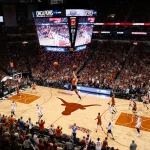 Texas player leaps into the air with the ball while confetti swirls over a packed arena and cheers erupt from the stands.