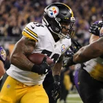 T.J. Watt breaks through a line of Ravens with Steelers jersey and a golden sunset glow on his helmet in a cheering stadium