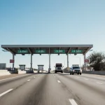 Vehicle axles crossing highway with wooden sign toll increases and clear blue Texas sky