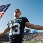 Trevor Lawrence celebrating with open arms and a waving American flag in front of cheering Jaguars fans under blue sky